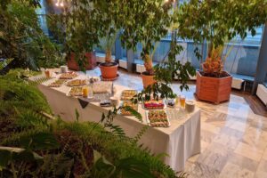 Catering bankietowy w otoczeniu roślin – eleganczne przekąski na tacach, soki i szkło do serwowania przygotowane przez Dworek Bobrza